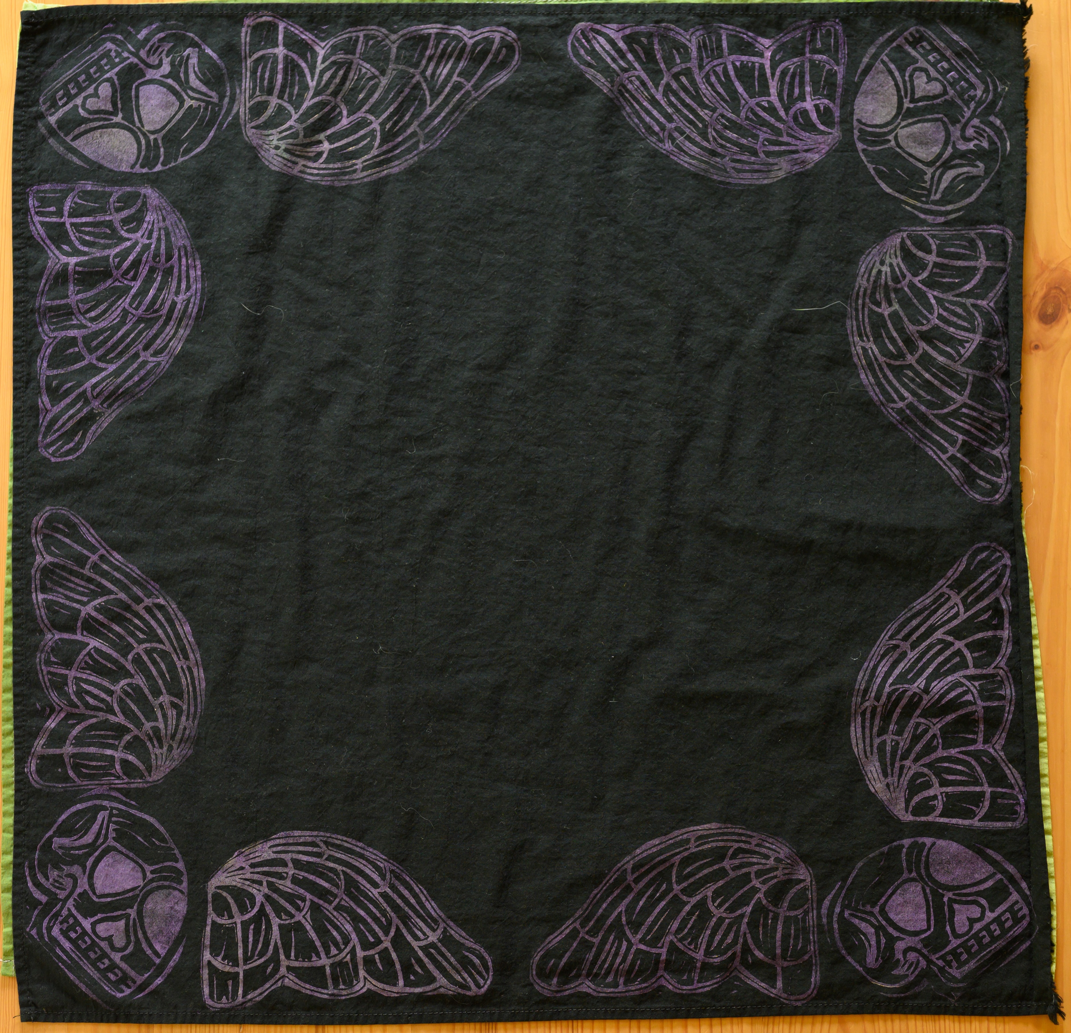 An overview of a black bandana. There is a pale purple death's head in each corner (skull with angelic wings), taking up essentially the border of the bandana.
