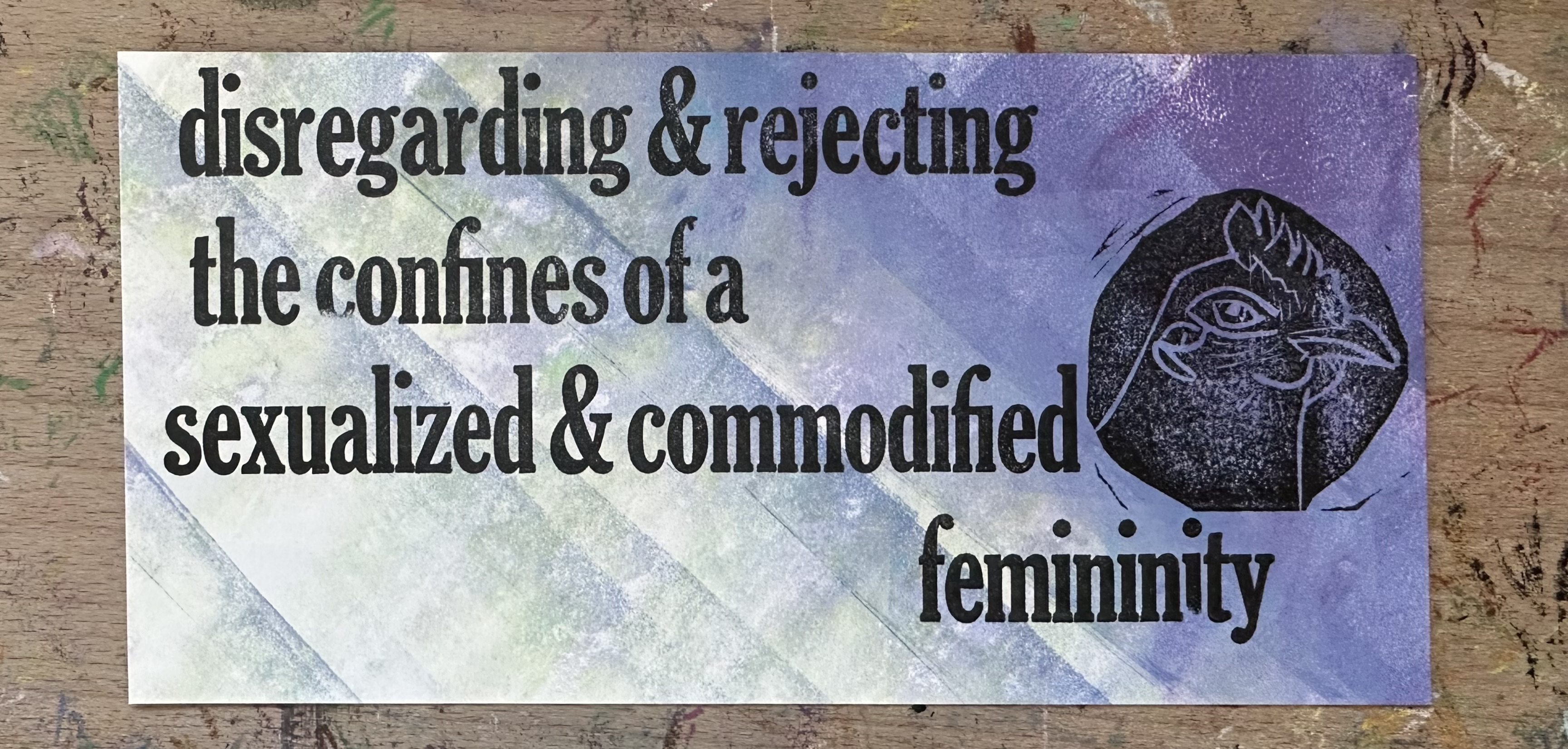 Rectangluar piece of white paper with diagonal chunky lines in gradient purple blue. In clear black text "disregarding & rejecting the confines of a sexualizied & commodified femininity" with a block print of a chicken's head in profile in a circle above.