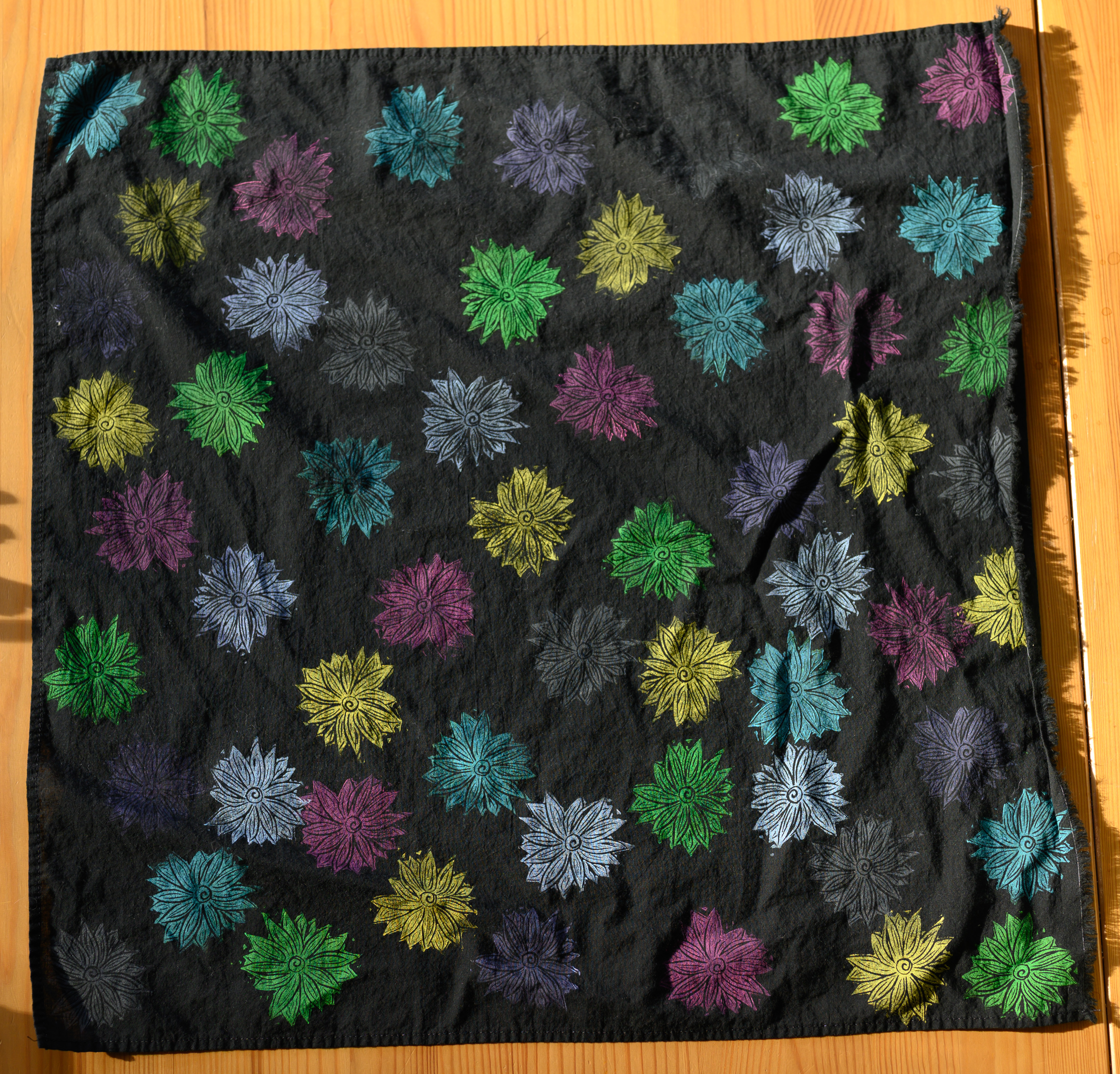 A close up of a black bandana from above covered in flowers. The flowers are all different colors.