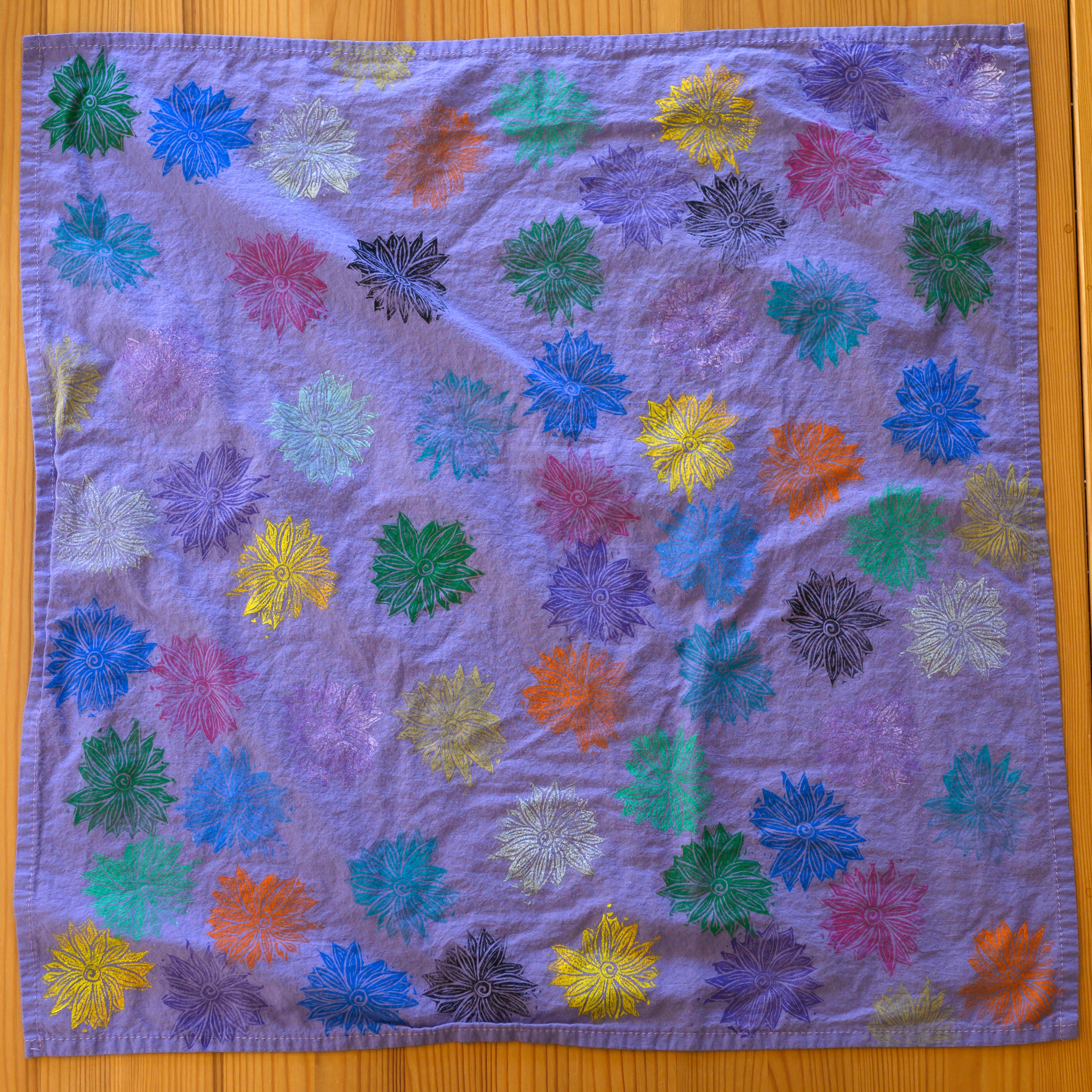 A close up of a purple bandana from above covered in flowers. The flowers are all different colors.