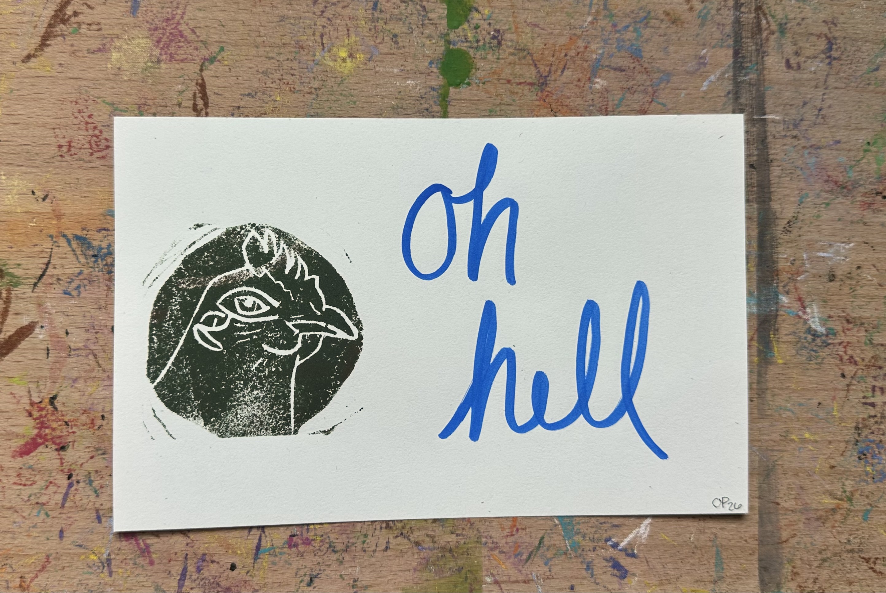 Rectangular piece of off white paper. A dark green/brown block print of a chicken in profile witha knowing look on the left. "oh hell" written on the right.