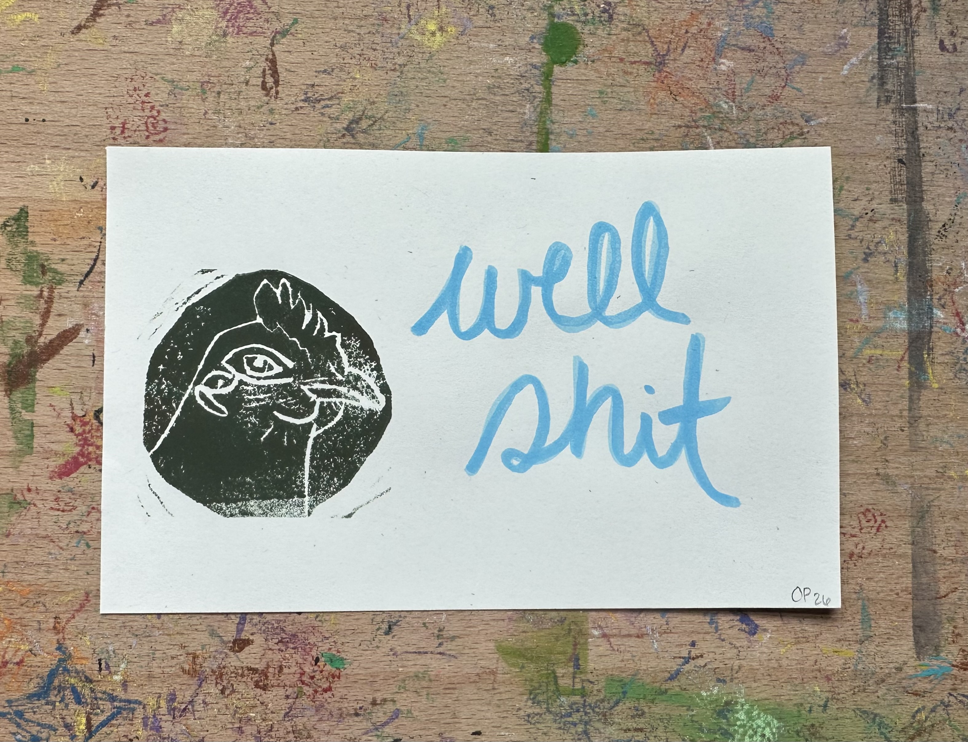 Rectangular piece of off white paper. A dark green/brown block print of a chicken in profile witha knowing look on the left. "well shit" written on the right.