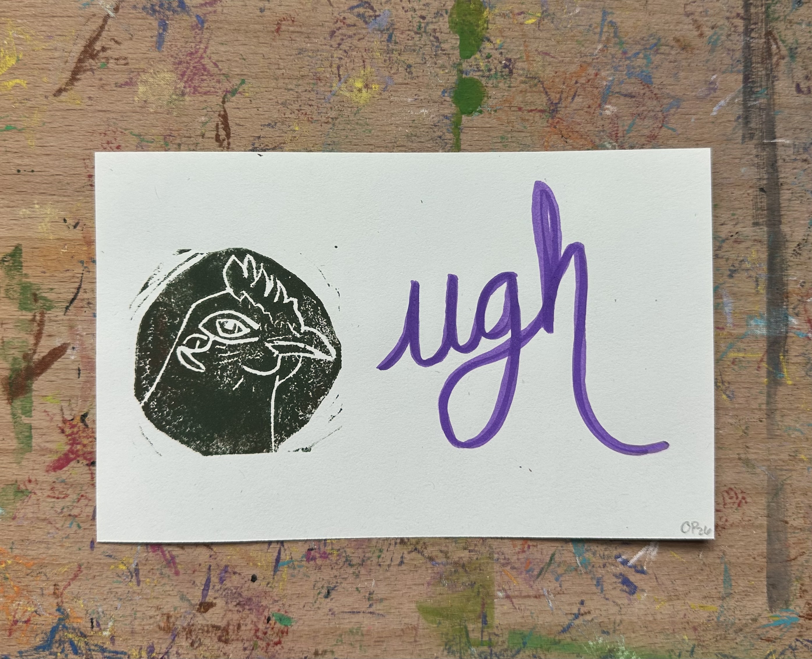Rectangular piece of off white paper. A dark green/brown block print of a chicken in profile witha knowing look on the left. "ugh" written on the right.