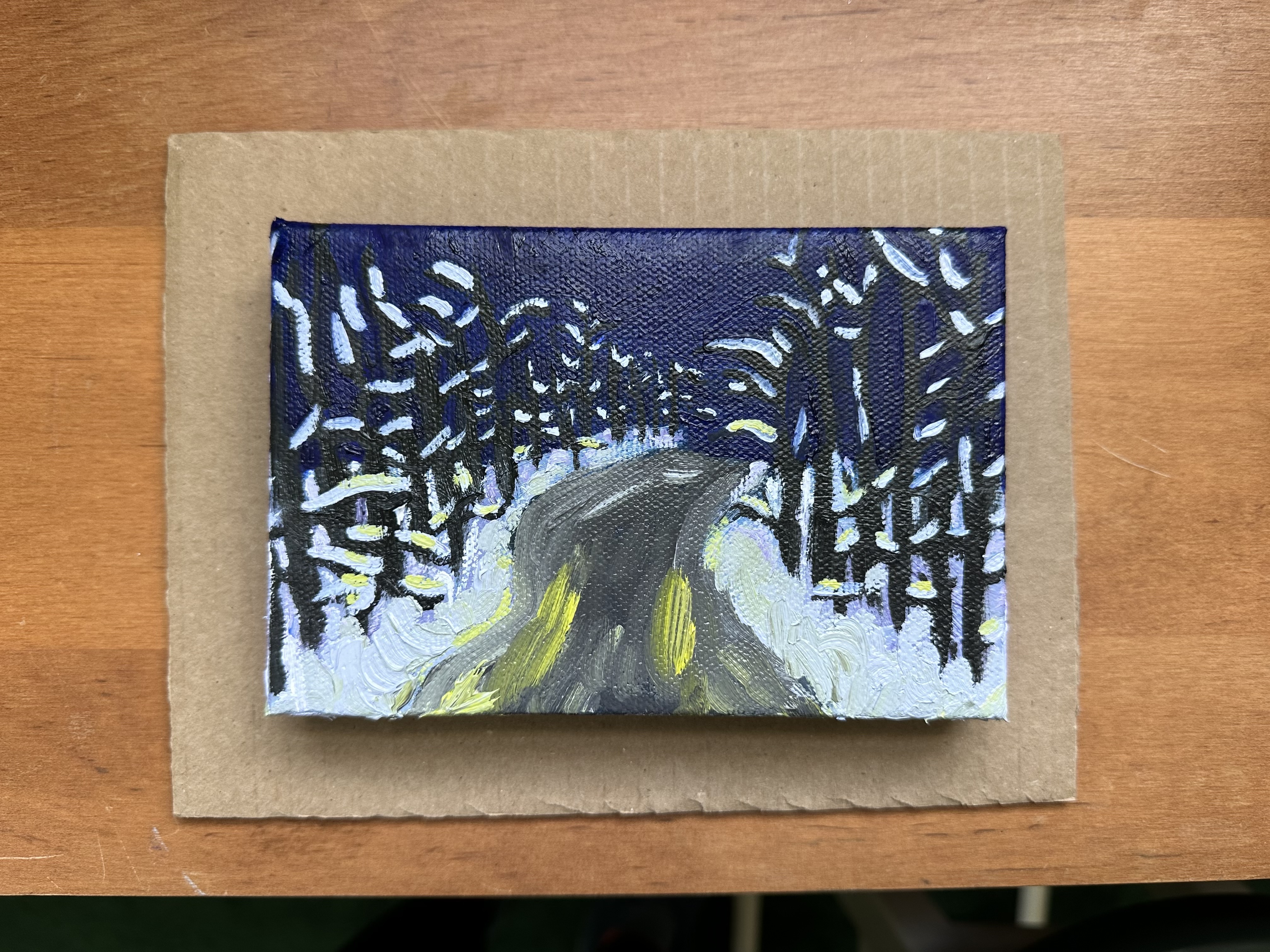 A curvy road goes into the distance in the center. There are stripes of yellow suggesting headlights. Around the road is snowy with snow covered trees. The sky is dark.