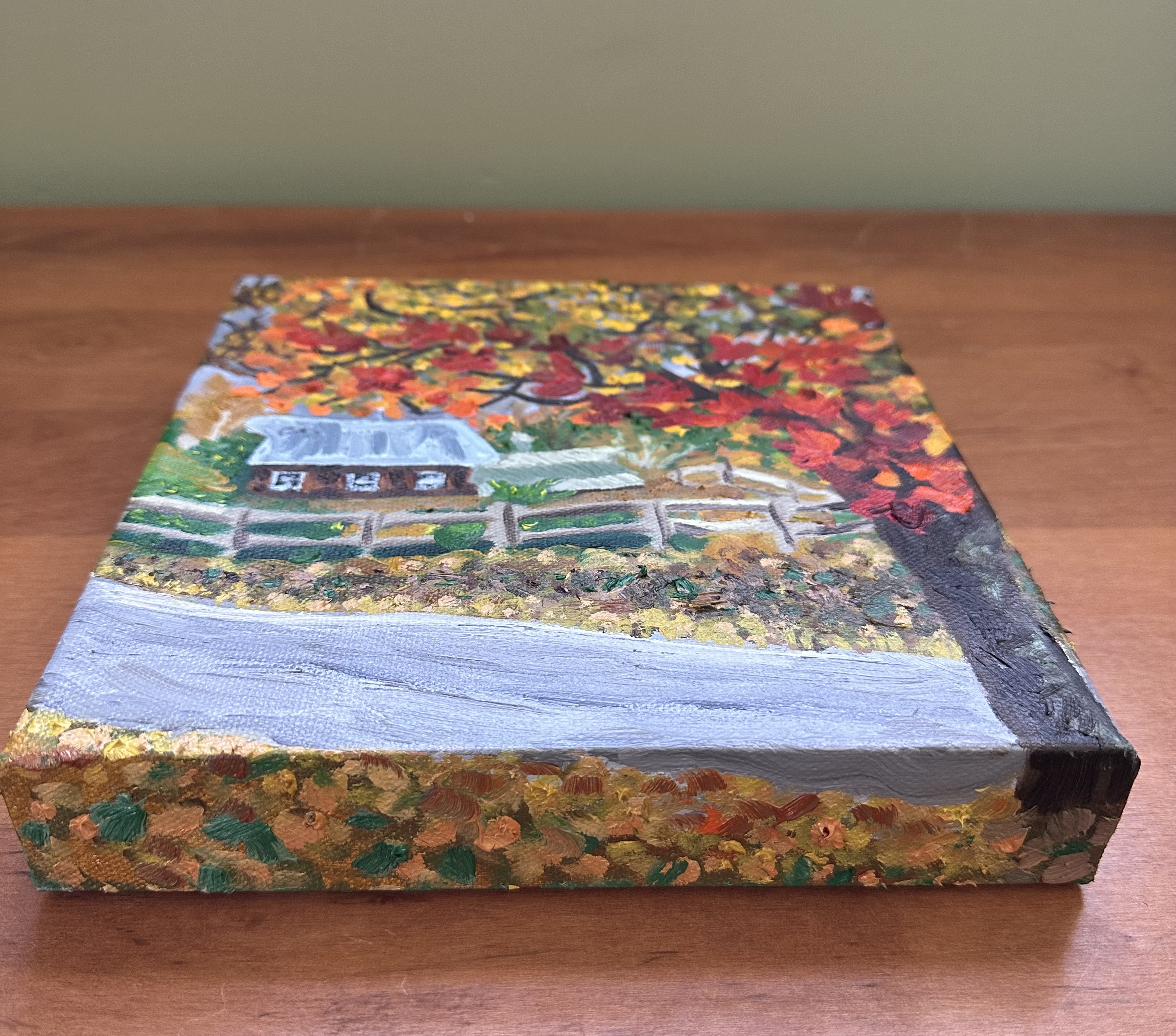 The bottom side of the painting with a partial view of the front. The bottom shows leaf covered ground, a little bit of the road, and a bit of the bottom of the tree.