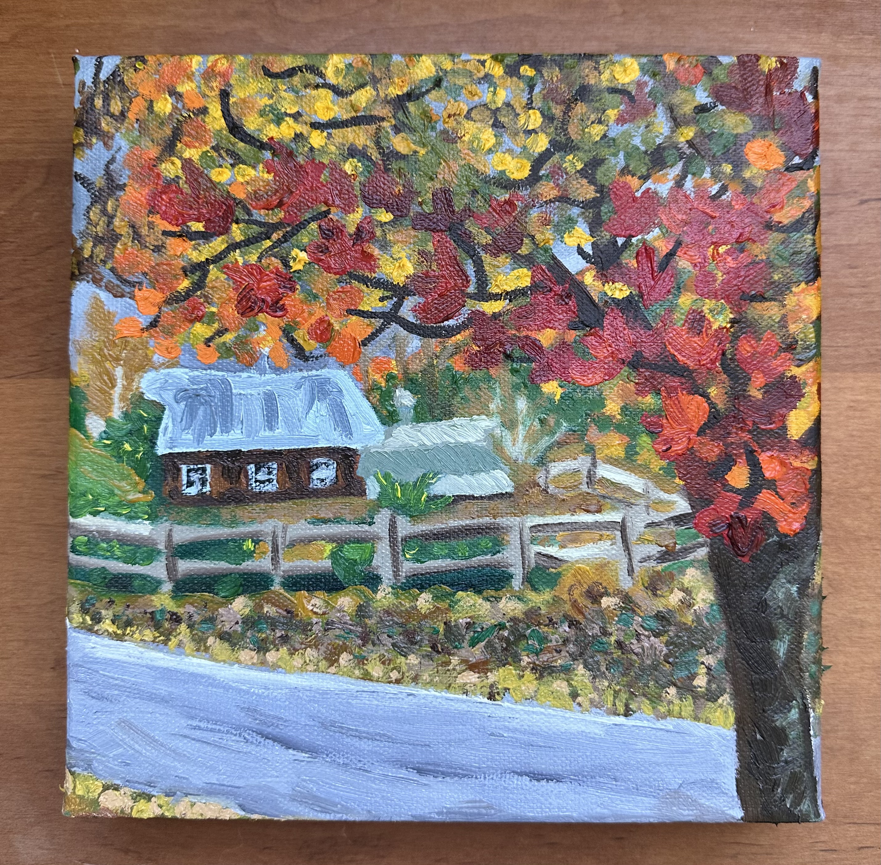 The front of the painting - there's a tree to the far right with it's branches and leaves stretching over the top in a variety of reds, yellows, oranges, and a little green. Below the branches are two barns in the distance - one is the full side and the other is further back so only the roof is seen. A wooden fence surrounds them. Closer to the tree is a road sloping from the left to right.