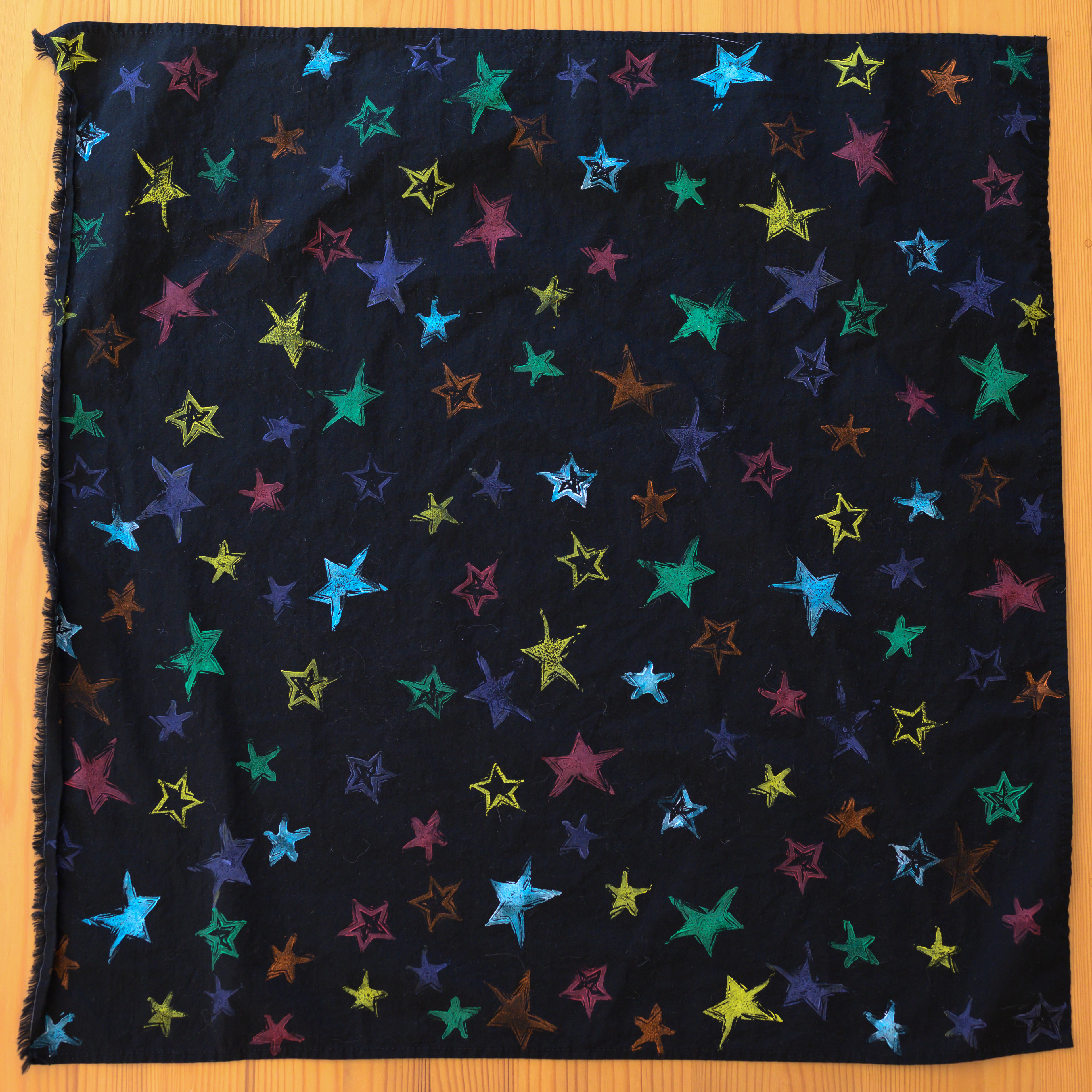 A black bandana from above. It is covered in stars of various colors and styles.