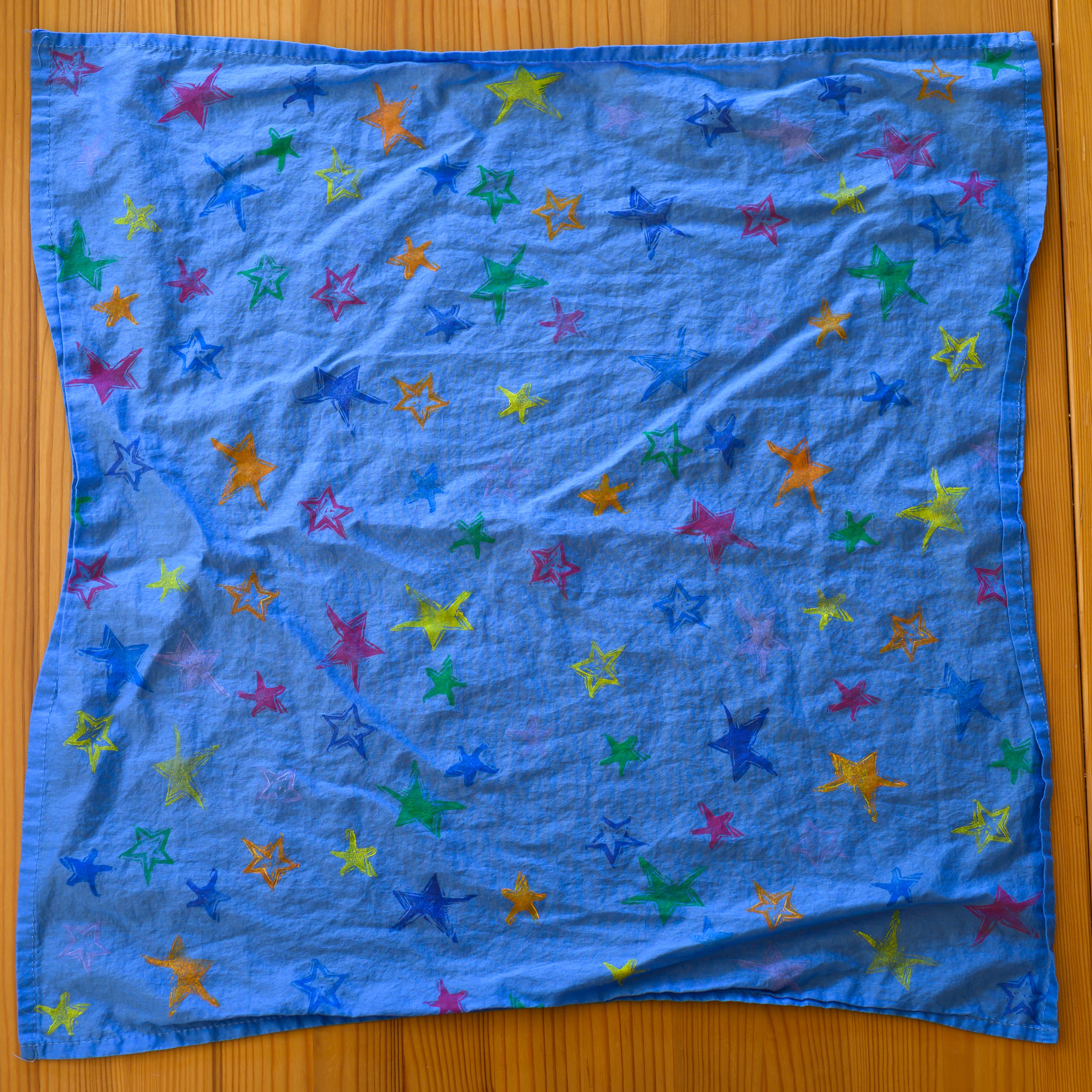 A periwinkle blue bandana from above. It is covered in stars of various colors and styles.