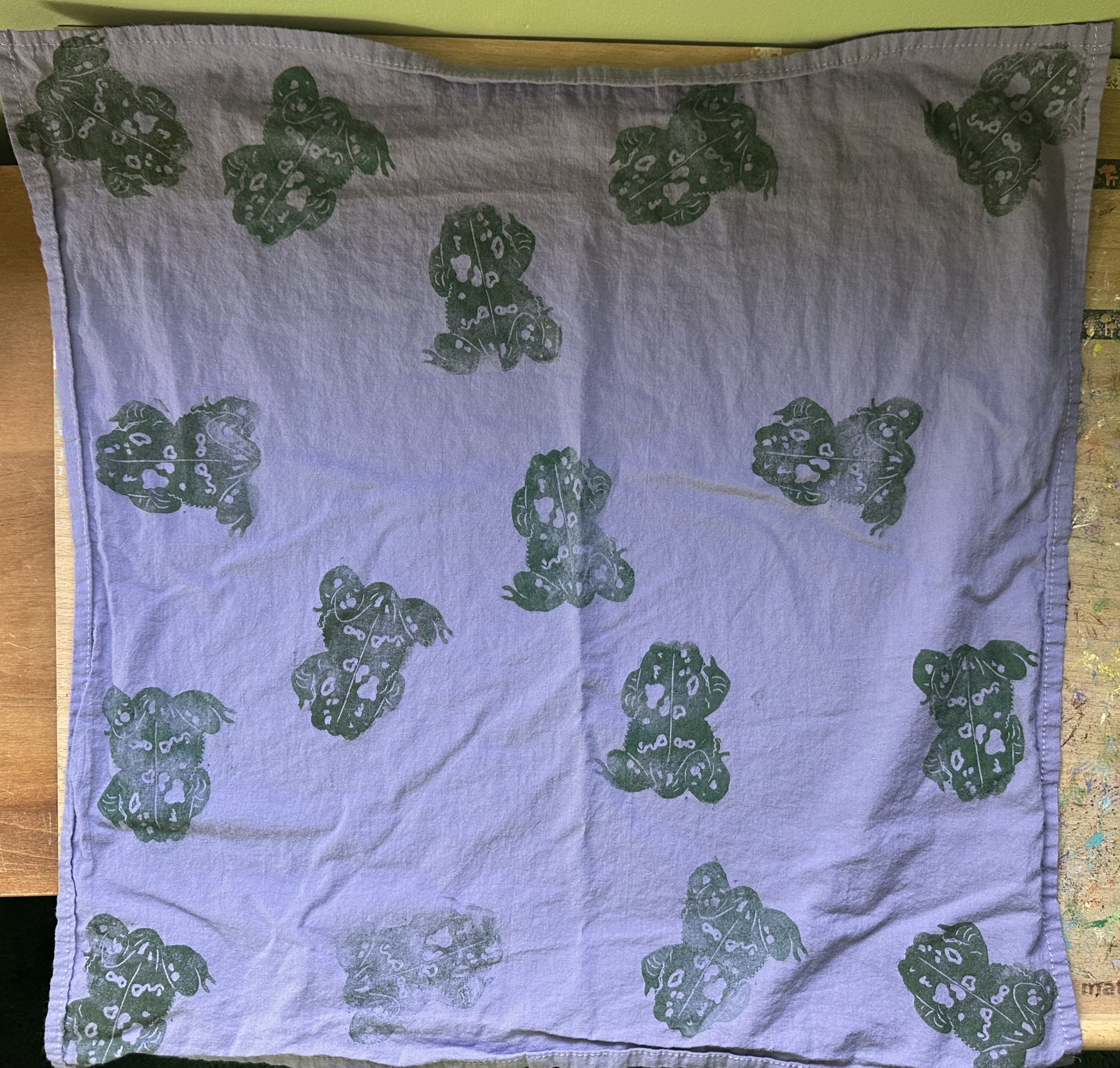 A light purple bandana from above covered in dark green toads.