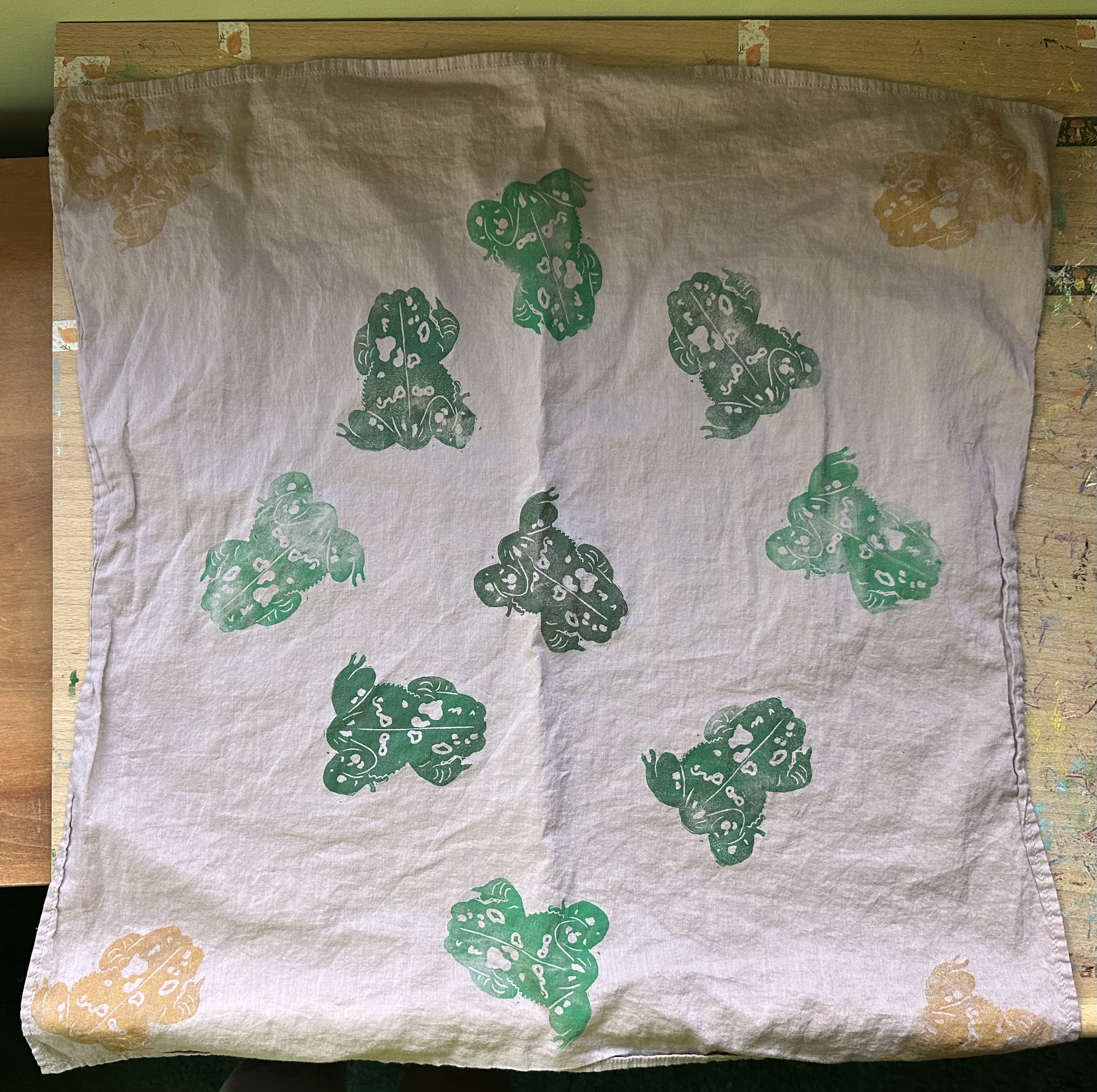 A dusky pink bandana from above with toads on it. Tan/brown ones in the corners and in the center is an assortment of green/brown ones.